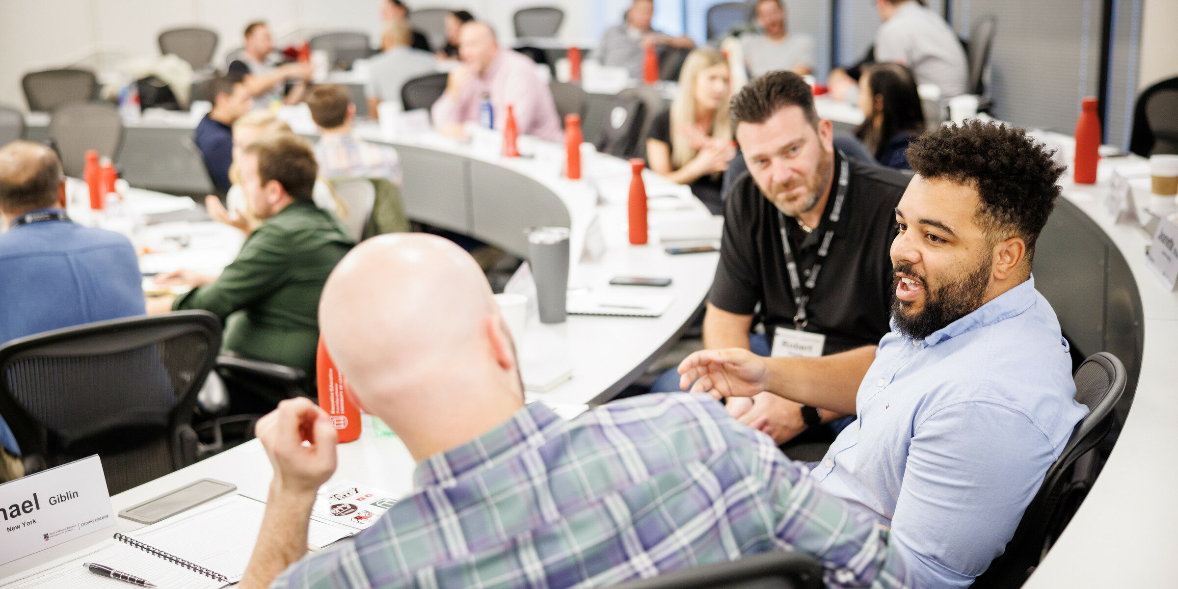 Three men talk to each other from their classroom seats during an event at the Terry Executive Education Center.