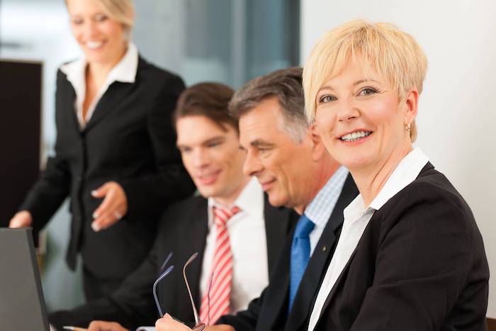 Four people in suits sit at a table during a business meeting.