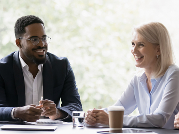 A man and woman in business attire smile as they talk during a meeting.