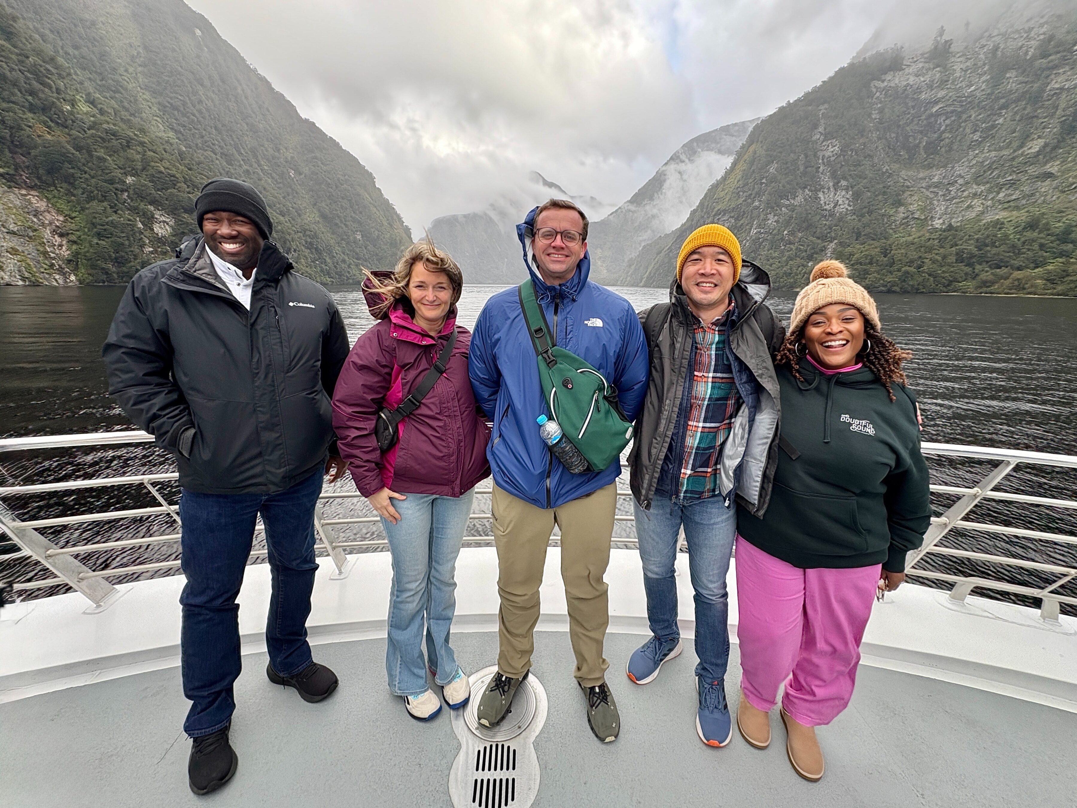 Terry College MBA students pose for a photo on a boat with a body of water and mountains in the background.