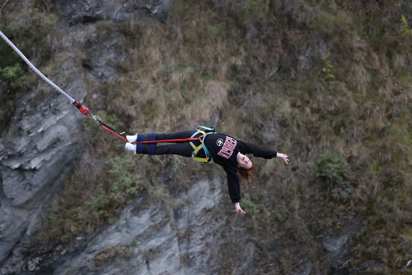 A female Terry College MBA student bungee jumps with a cliff side in the background.