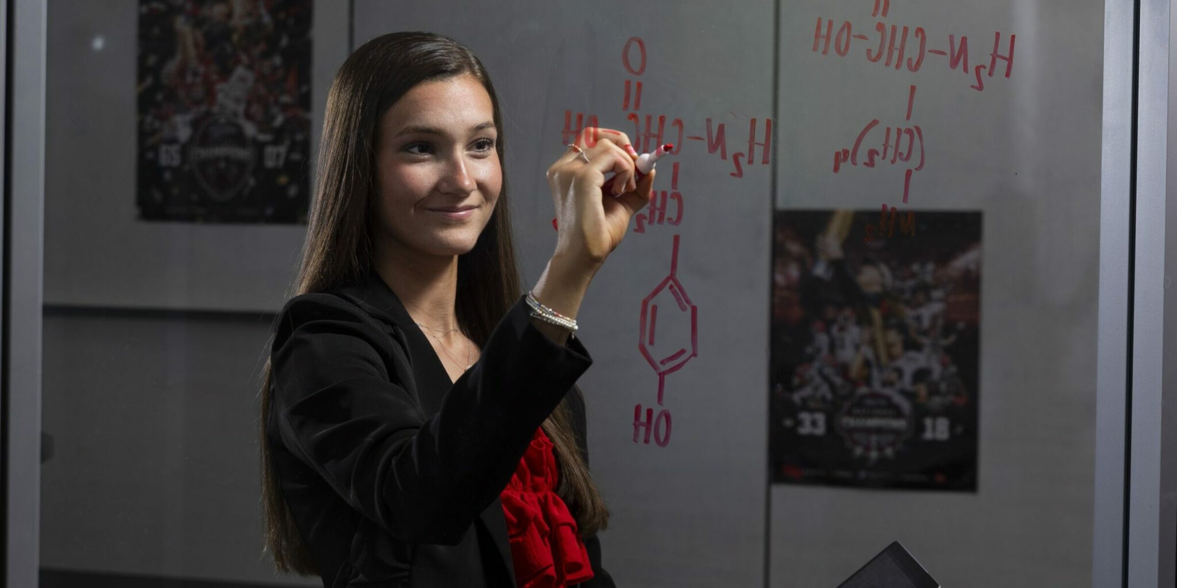 Halle Bynum works chemistry problems on a transparent white board.