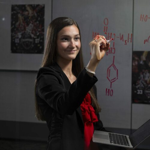 Halle Bynum works chemistry problems on a transparent white board.