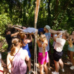 multiples students support the weight of a fellow student as they pass him through ropes during a teambuilding exercise