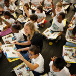 female college student sits among numerous elementary school kids with open books