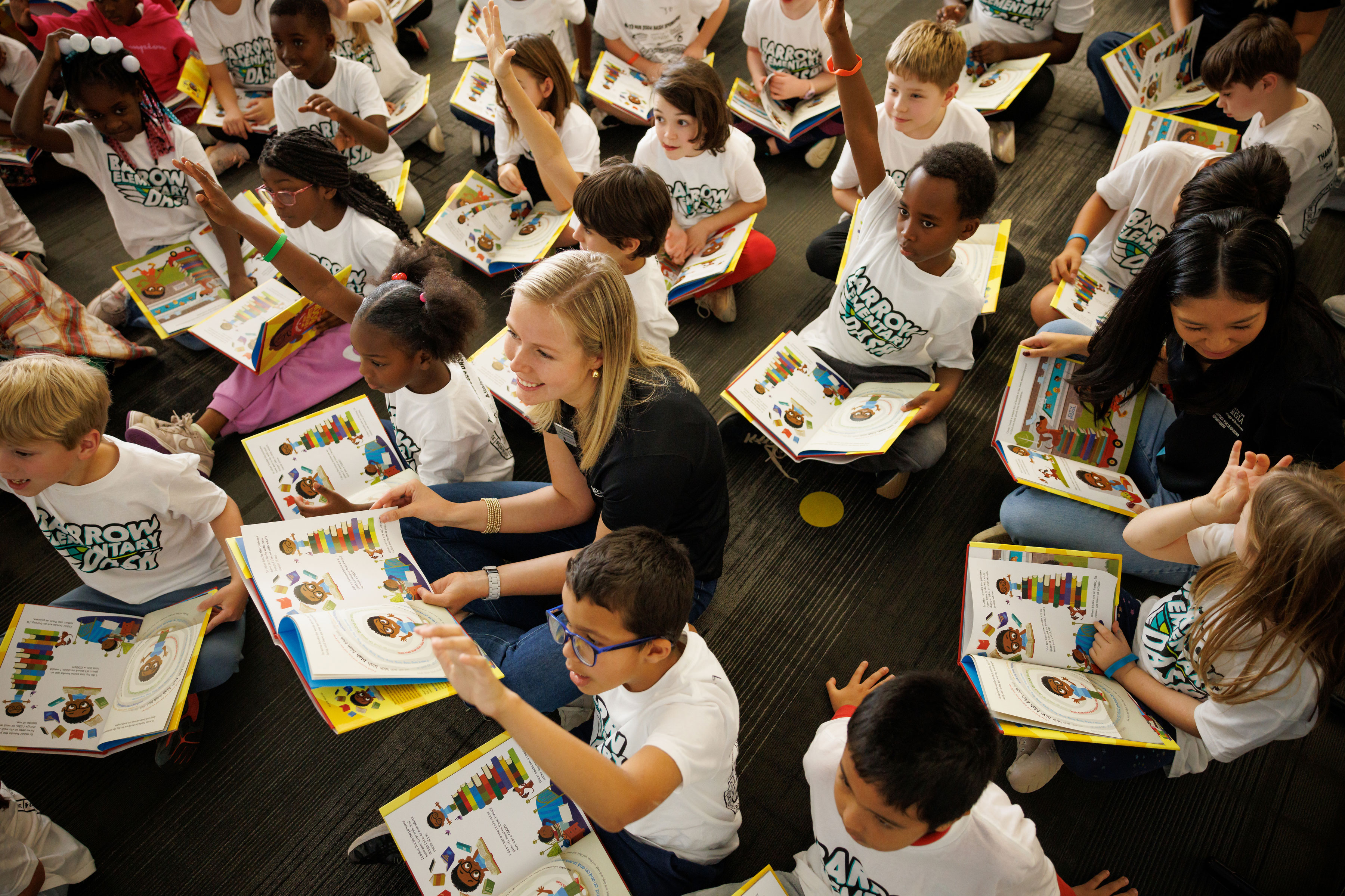 female college student sits among numerous elementary school kids with open books
