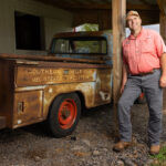 man poses next to vintage pickup truck