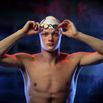 male swimmer wearing swim cap lifting goggles from face
