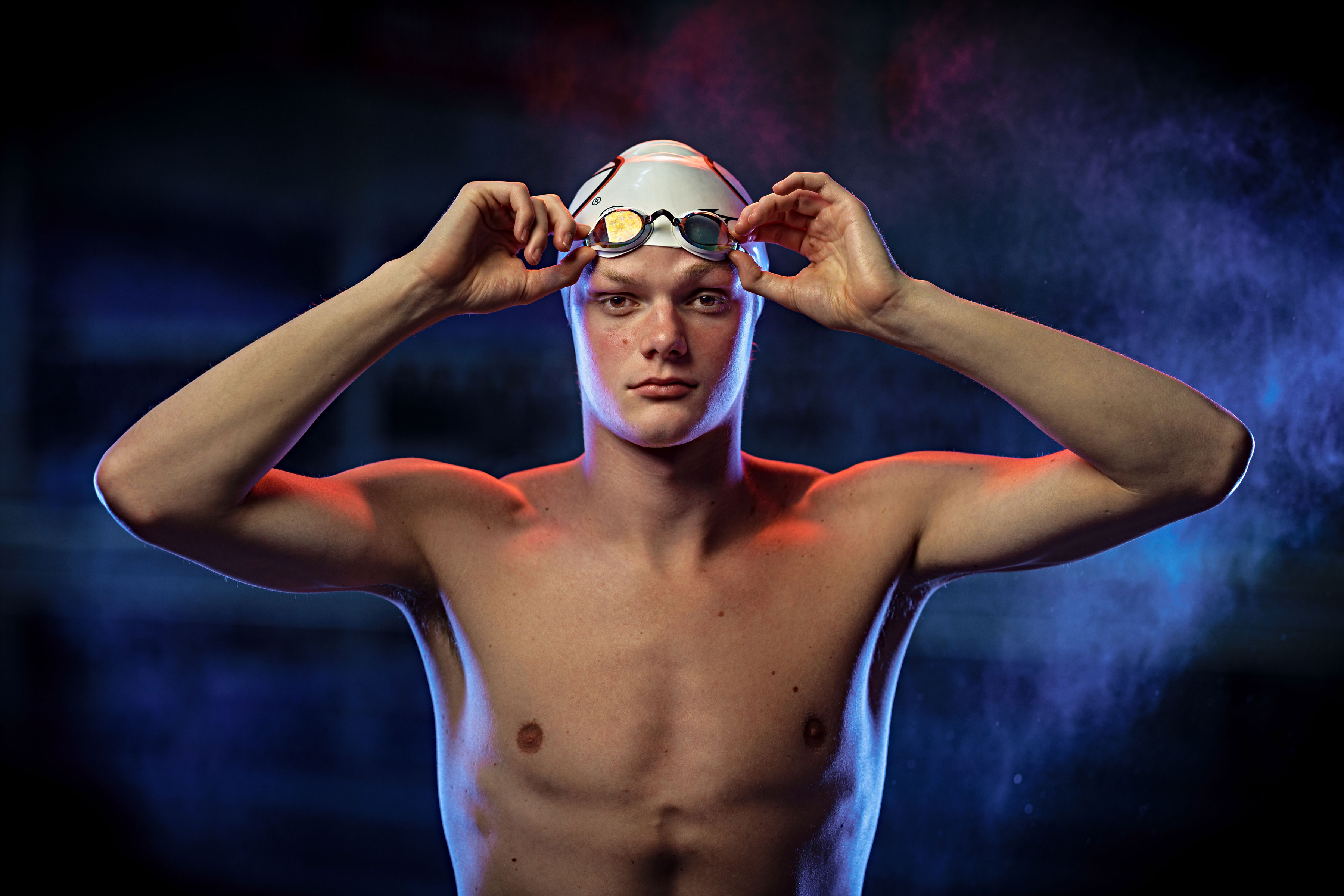 male swimmer wearing swim cap lifting goggles from face