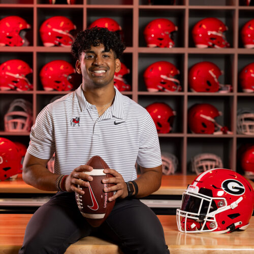 Jayan Patel holds a football in front of shelves of red football helmets
