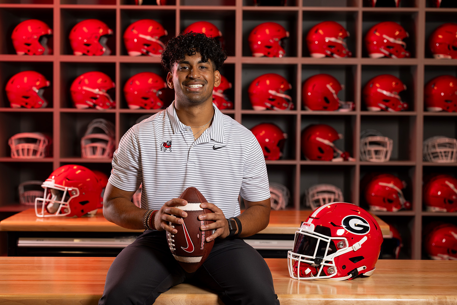 Jayan Patel holds a football in front of shelves of red football helmets