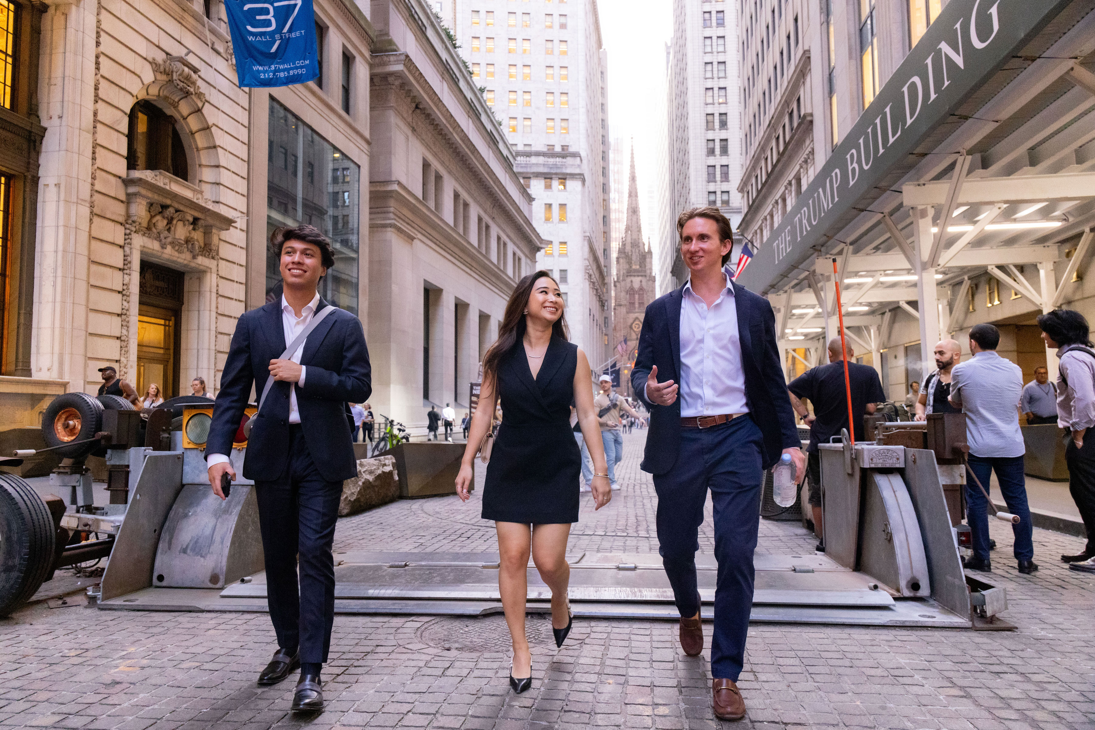 three young adults walk in front of the New York Stock Exchange in business attire