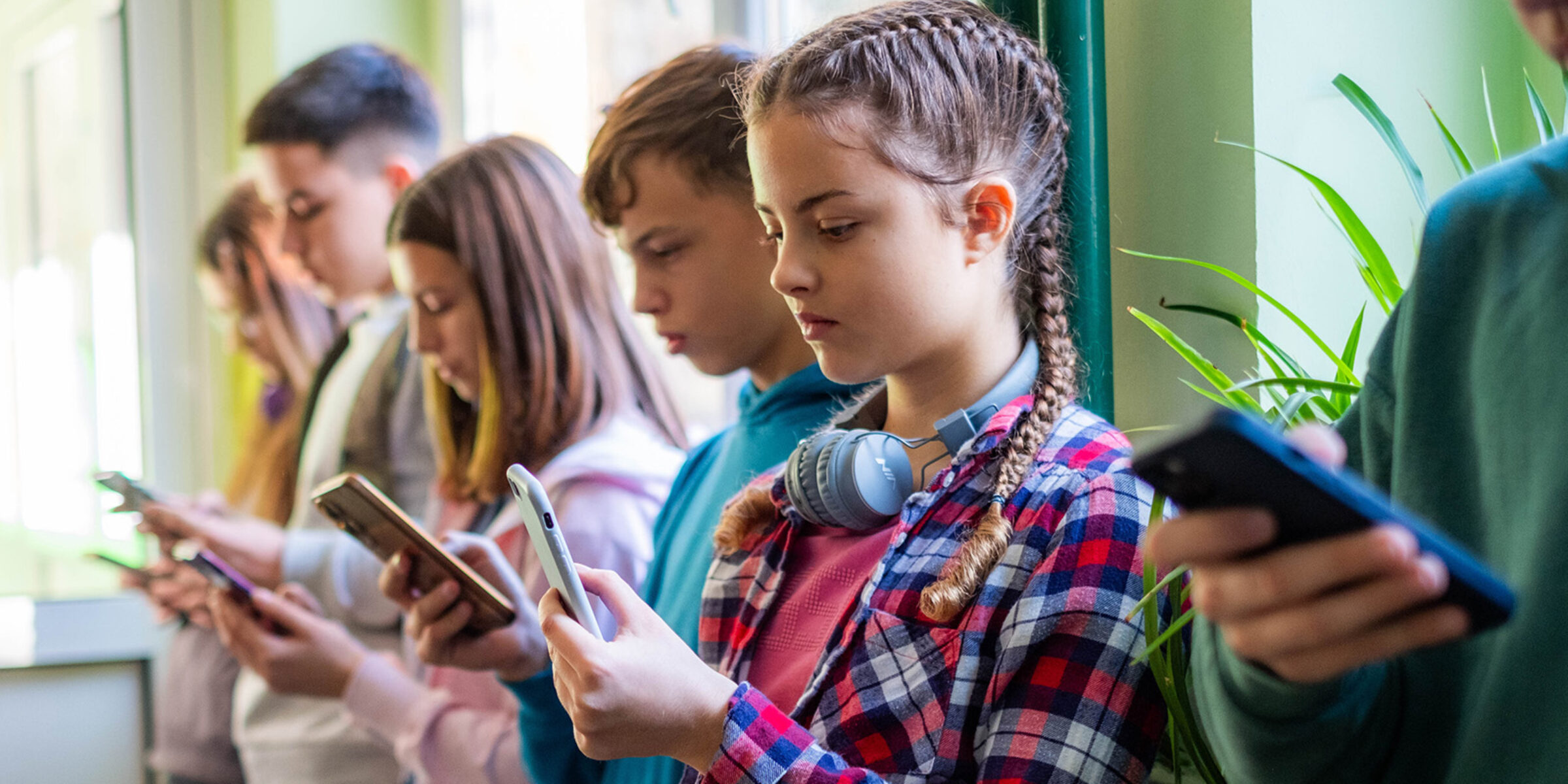 Middle School students stand against a wall, all staring at their phones Will Meta’s mega-settlement change social media?