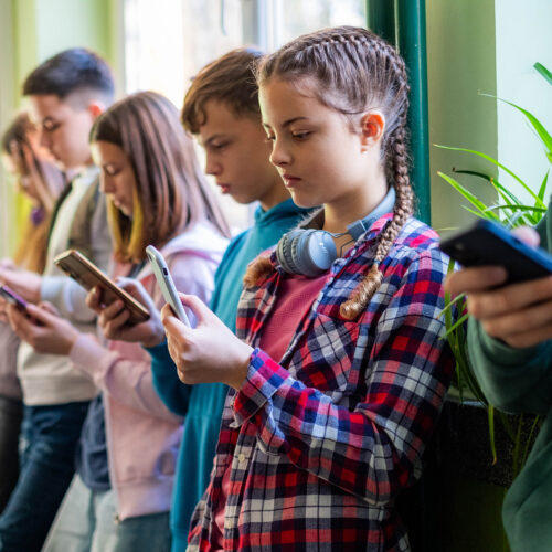 Middle School students stand against a wall, all staring at their phones Will Meta’s mega-settlement change social media?