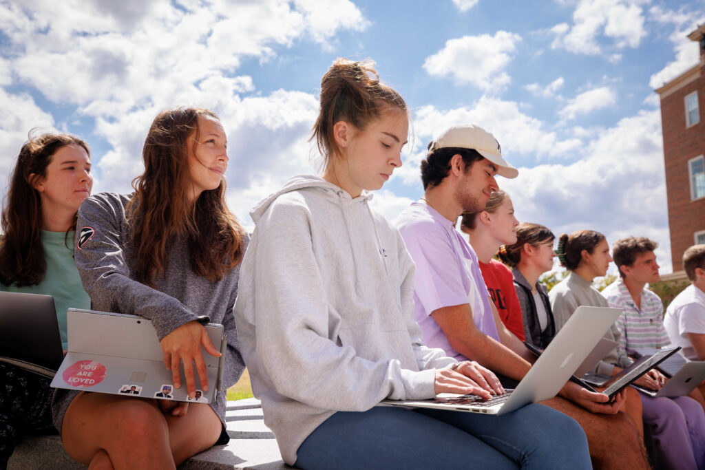 Terry College students sit outside on a sunny day while using their laptops during an outdoor lecture.