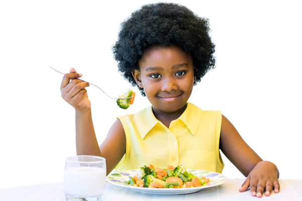 A child picks up a piece of broccoli from her plate with a fork.