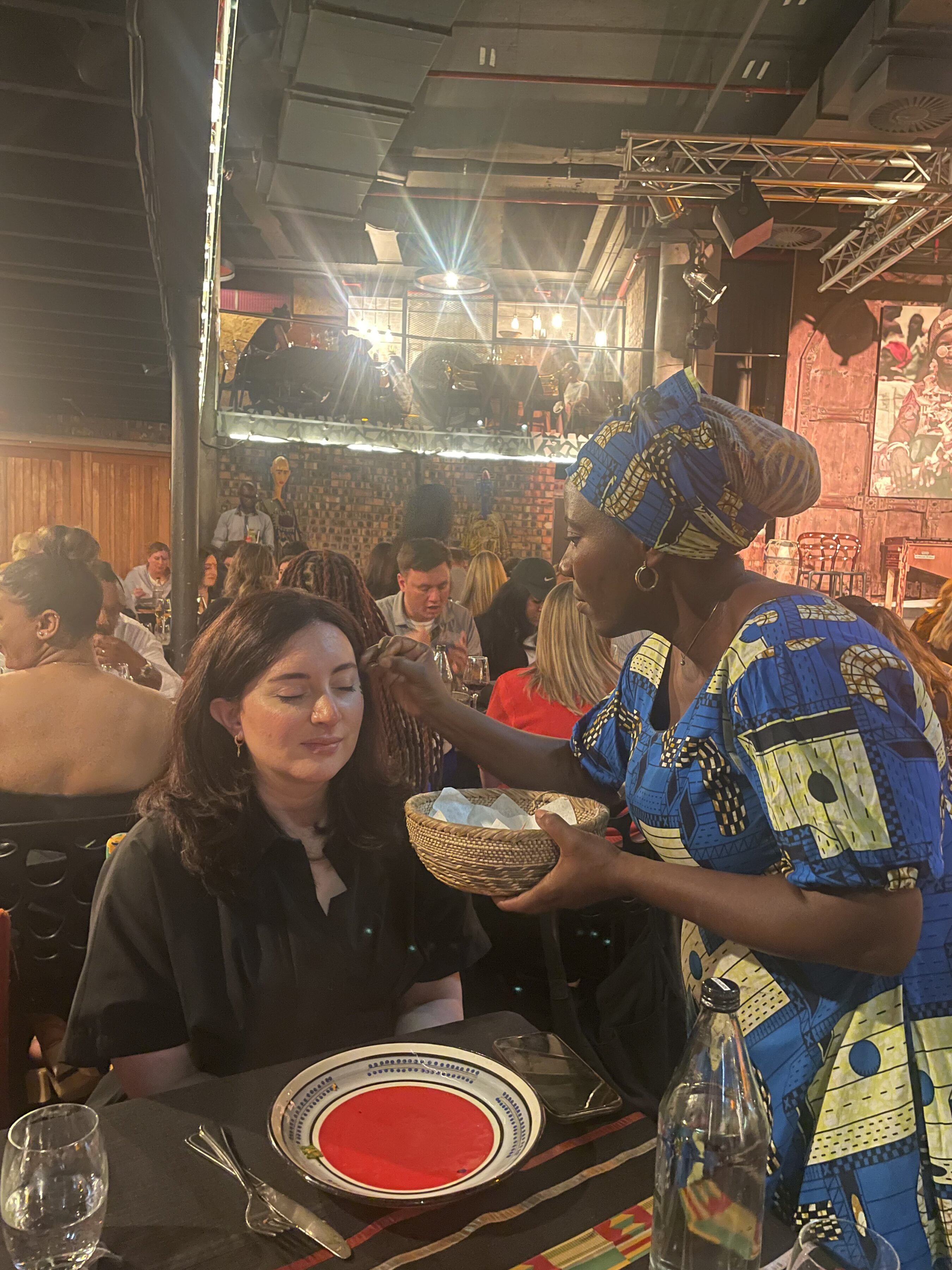 A woman in traditional South African attire paints the face of a Terry College MBA student.