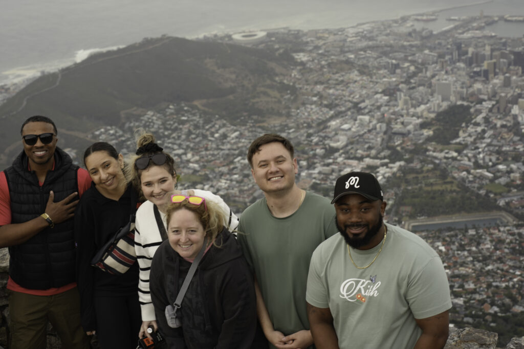 Terry College MBA students pose for a photo on a hillside with a city skyline behind them.