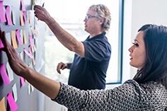 A man and woman collaborating on a wall covered in sticky notes, brainstorming and organizing ideas.