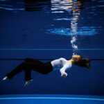 a woman wearing normal clothing while underwater lying parallel to ground