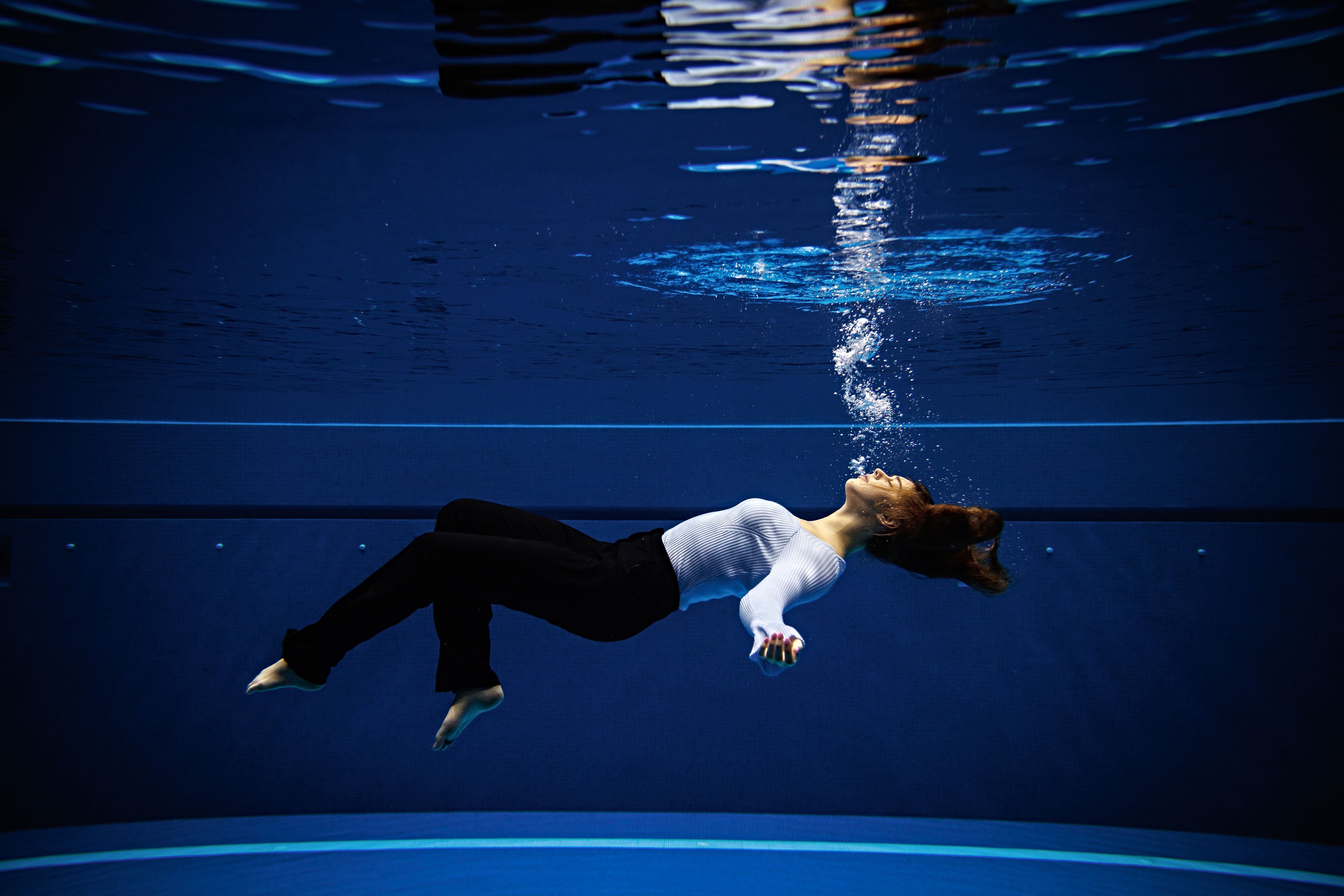 a woman wearing normal clothing while underwater lying parallel to ground