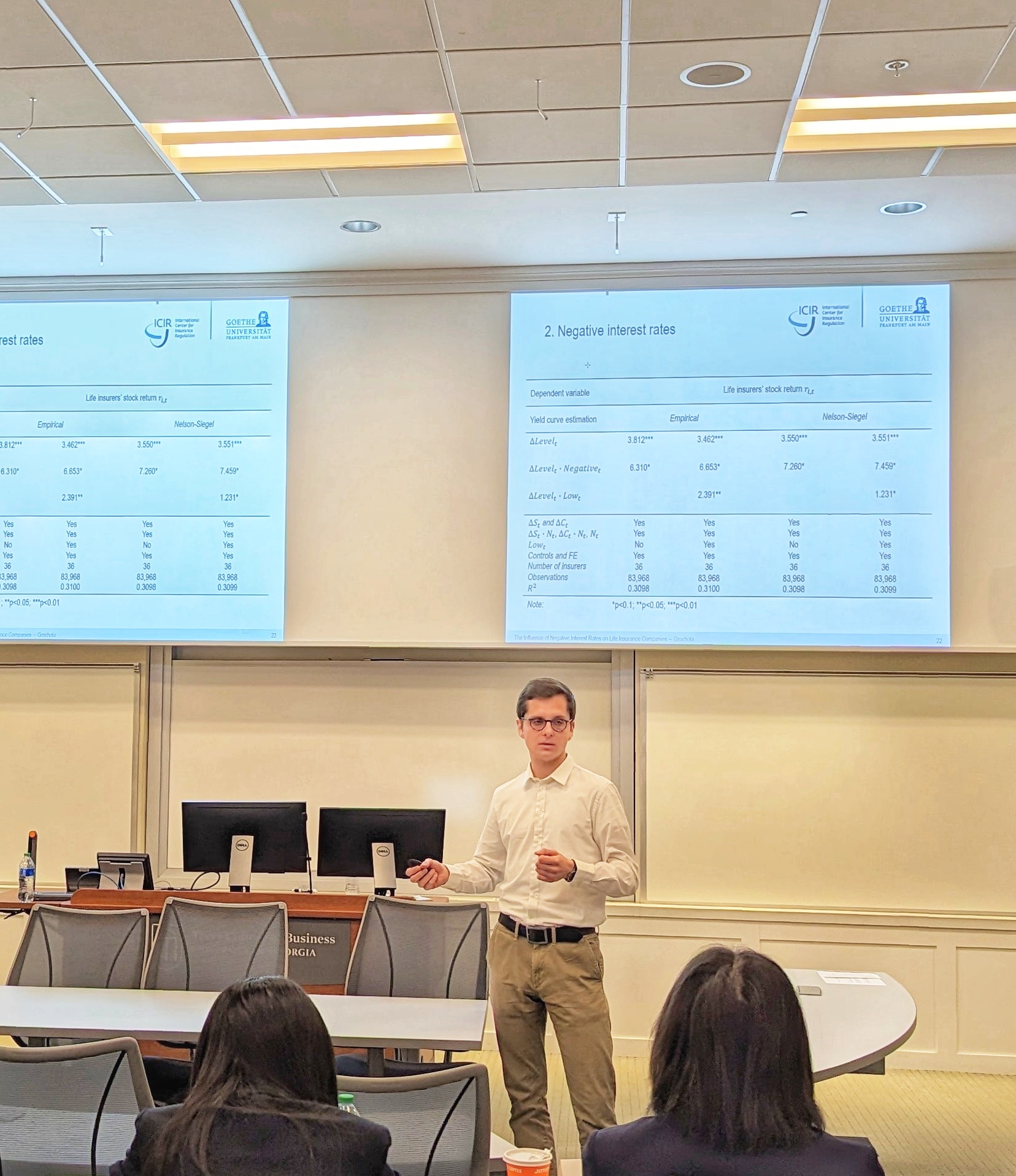 A male speaker talks to the audience in front of a presentation screen during a Risk Management & Insurance Symposium in a BLC classroom.