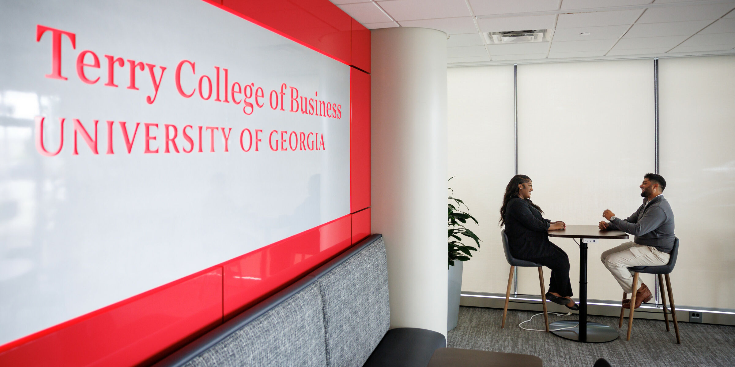 A man and a woman sit a table next a Terry College of Business sign inside the Terry Executive Education Center in Atlanta.