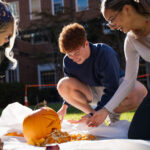 three college students carving pumpkin on lawn