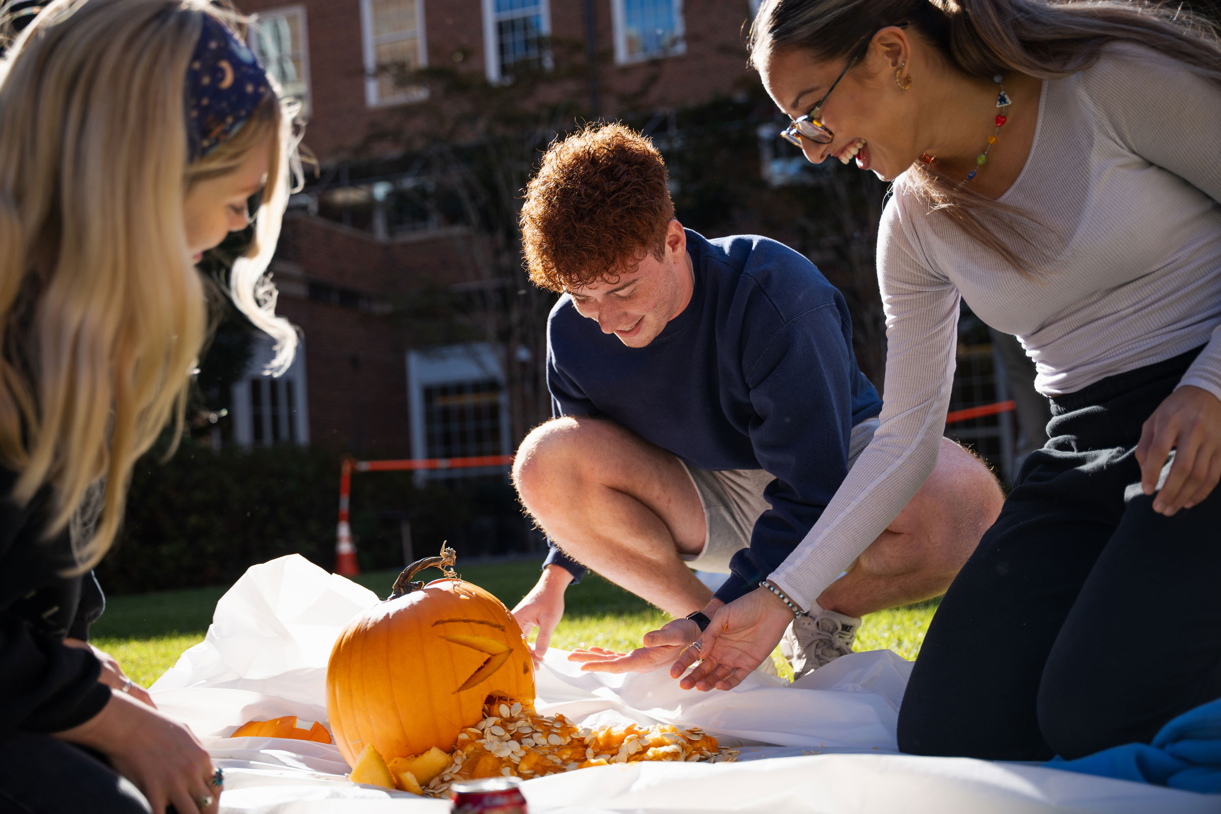 three college students carving pumpkin on lawn